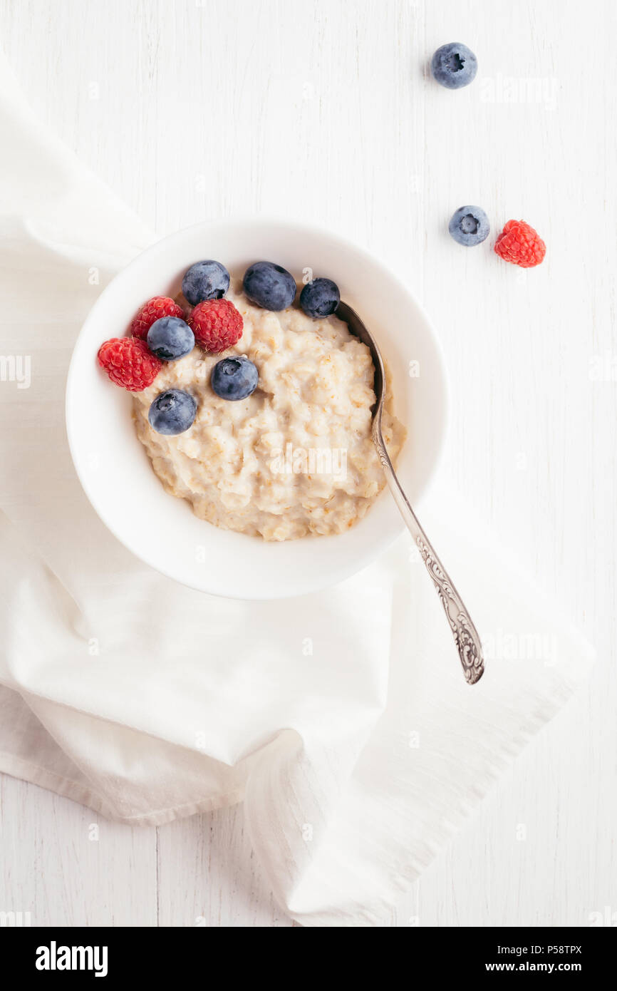 Eine Schüssel Haferflocken Haferflocken mit Heidelbeeren und Himbeeren auf weissem Holztisch. Ansicht von oben. Stockfoto