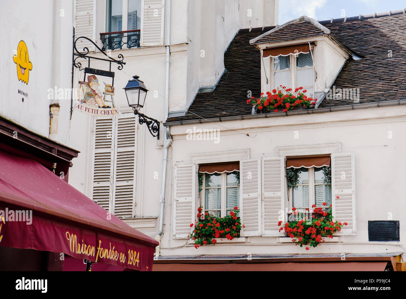 Paris, Frankreich, 10. August 2017. Typische Pariser Mansarde windows auf White Apartment französische Gebäude mit Dachgeschoss, Fensterläden und Ziegeldach mit roten Geranien Stockfoto