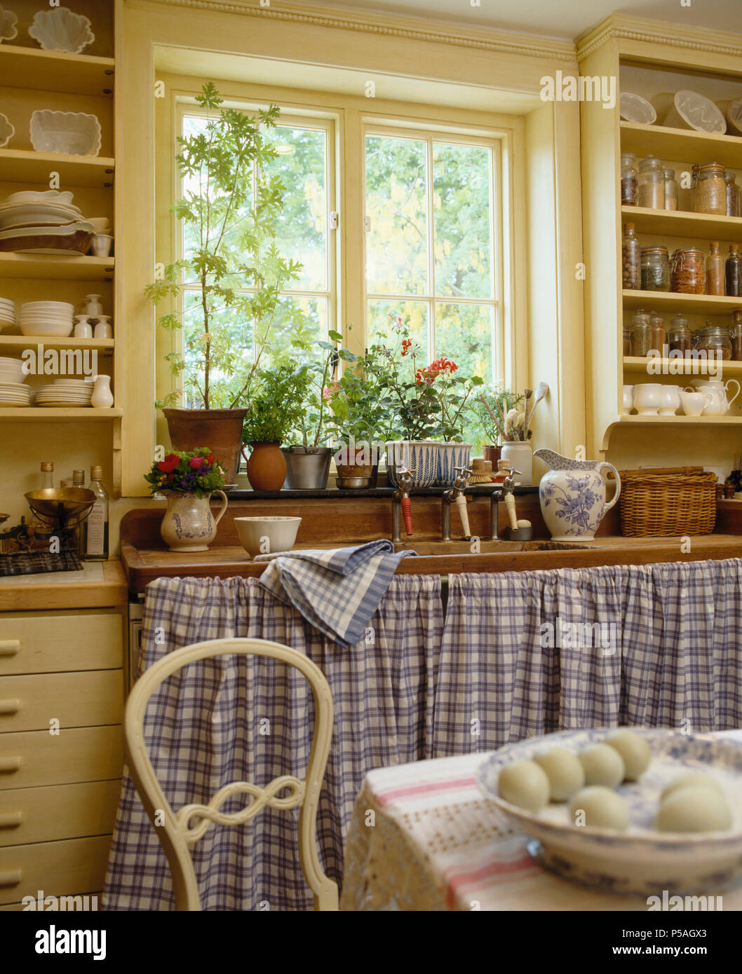 Blau karierte Vorhänge an Schränken unter Fenster in Cottage Küche Stockfoto