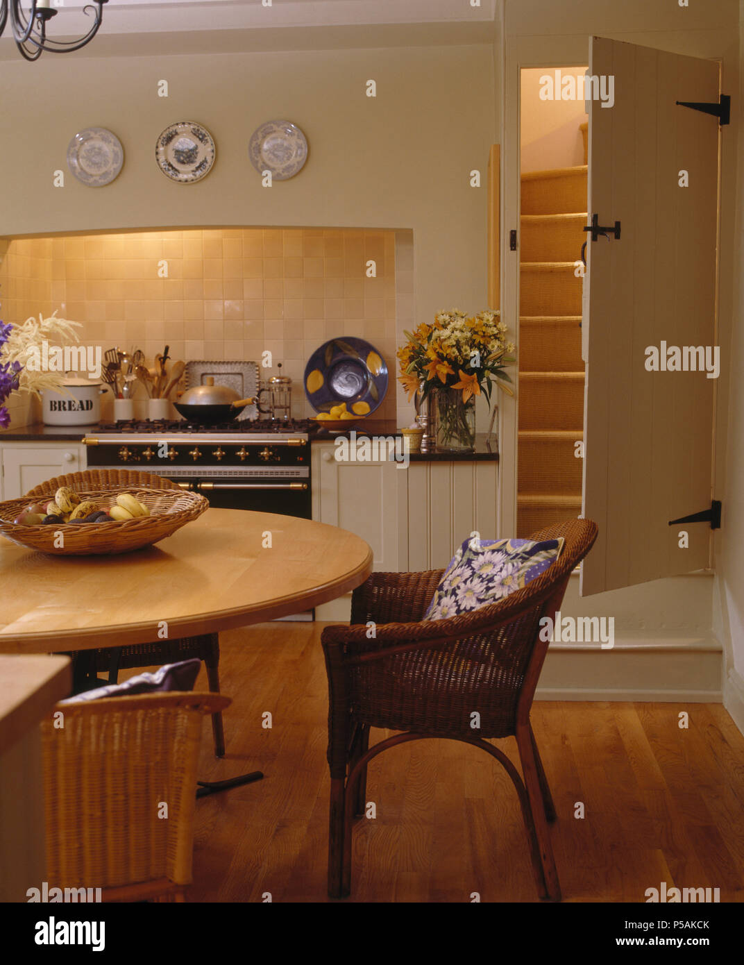 Korbstuhl in hellem Holz Tisch im Cottage Küche mit offener Tür neben dem Bereich Backofen auf Treppe Stockfoto