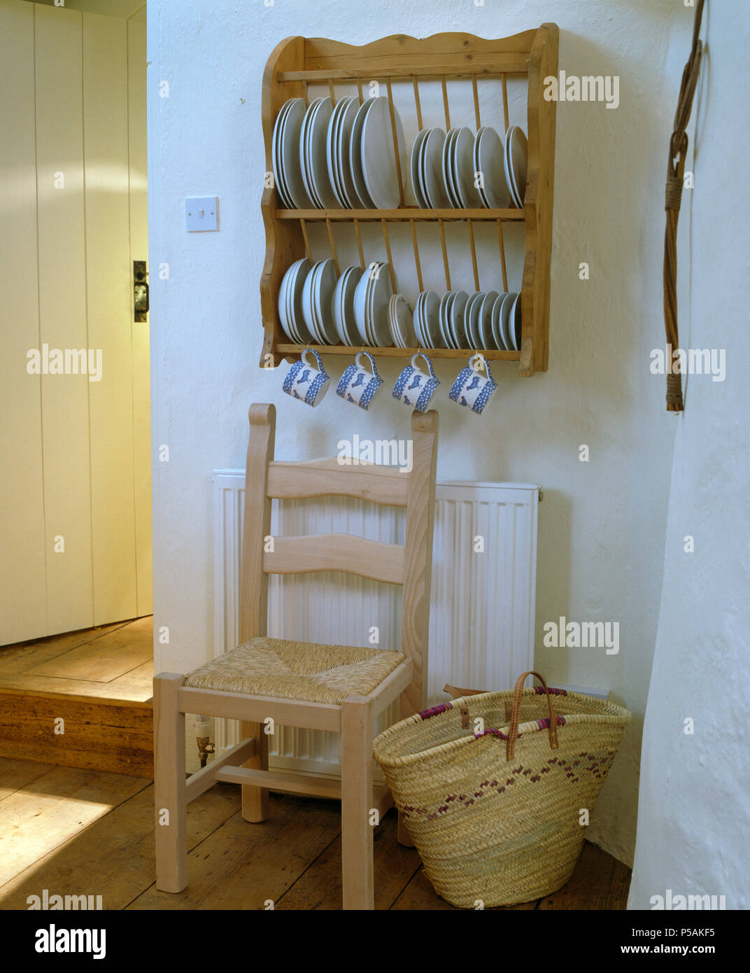 Weiße Platten auf Pine platte Rack über Rush sitzen Sessel und Bast Korb incottage Küche mit raffia Korb Stockfoto