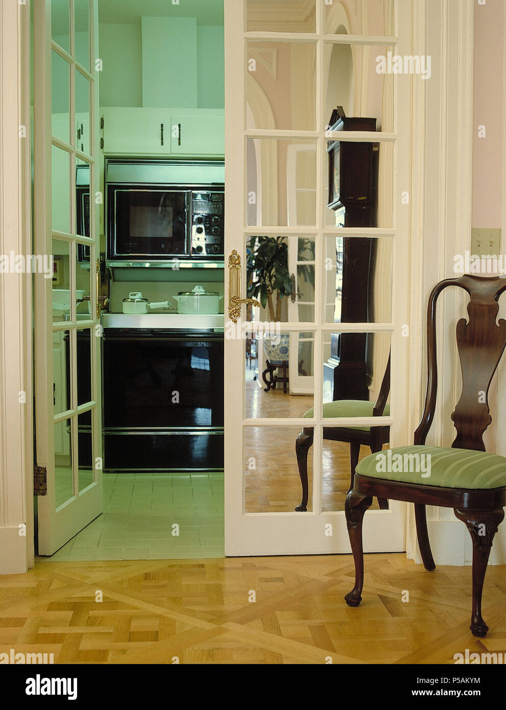 Vintasge Stuhl und Parkettboden in Halle mit gespiegelten Doppelzimmer mit Französischen Türen zu Küche über Stockfoto