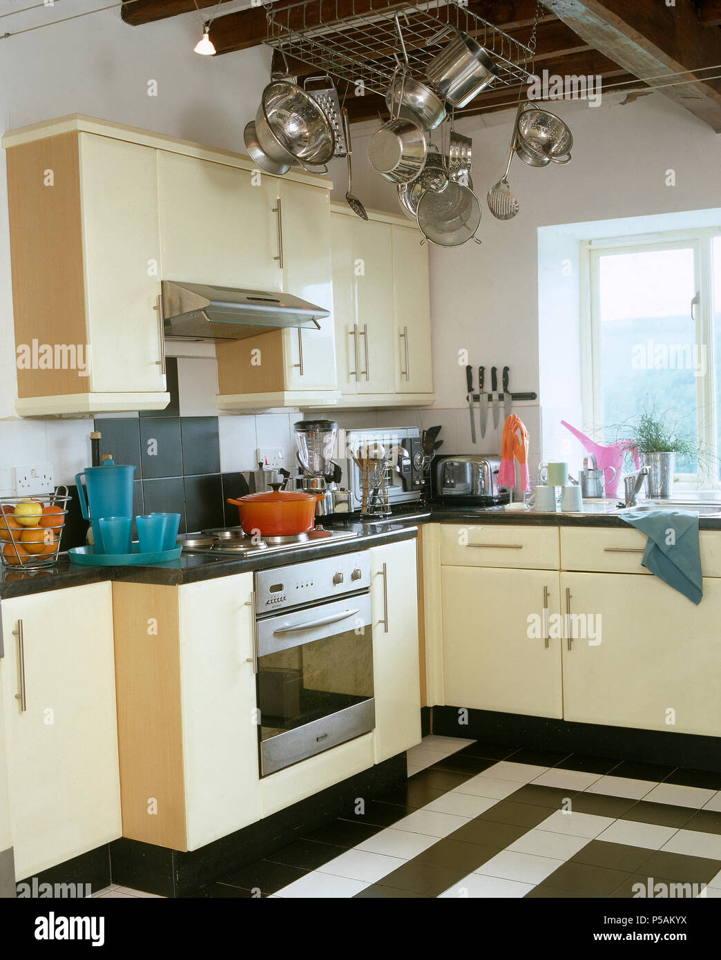 Hellen cremefarbenen Einheiten und schwarz-weißen Fliesenboden in der modernen Küche mit Edelstahl Pfannen auf Decke Rack Stockfoto