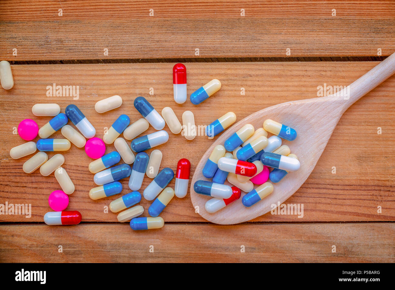 Bunte Pillen und Medikamente in einem hölzernen Kochlöffel, auf Holzplanken Hintergrund, Gesundheit und Medikamente Konzept Stockfoto