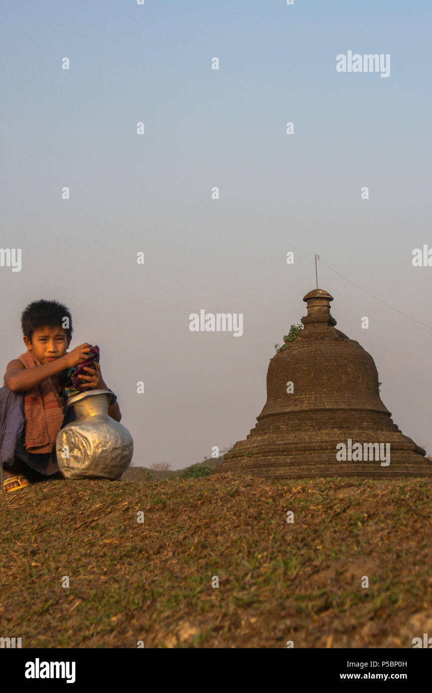 Junge mit seinem Wasser Topf mit Tempel als Hintergrund saß, Mrauk u Myanmar Stockfoto