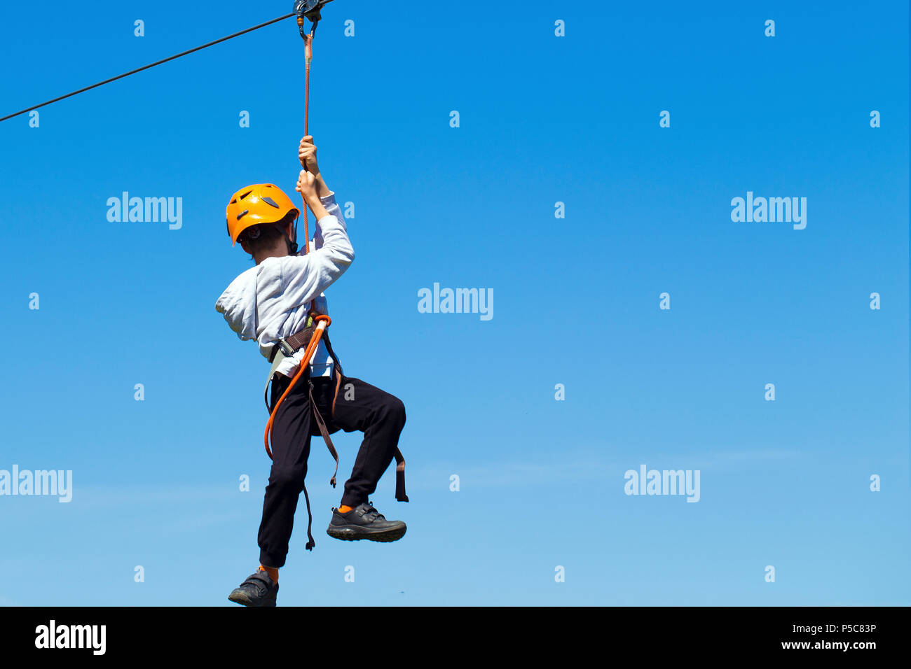Ein nicht identifizierter Junge in orange Helm, auf Tarzan vor blauem Himmel Hintergrund Stockfoto