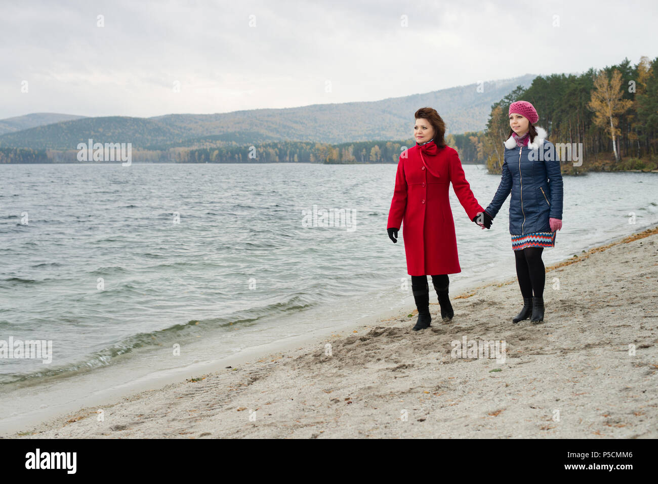Schönheit, reife Frau in Rot Topcoat mit jungen Tochter, Wandern outdoor auf dem Wasser Anlegeplatz für Boot, im Herbst kalt Bewölkter Tag Stockfoto