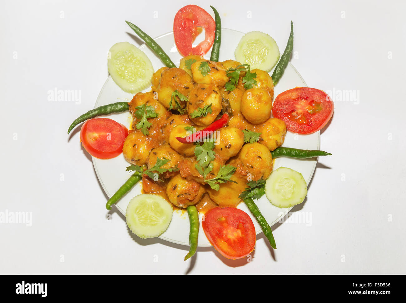 Scharfe Indische vegetarische Speisen zubereitet mit kleinen Kartoffeln im Volksmund bekannt als Dum Aloo mit Gurken, Tomaten und grüne Chilischote garniert. Stockfoto