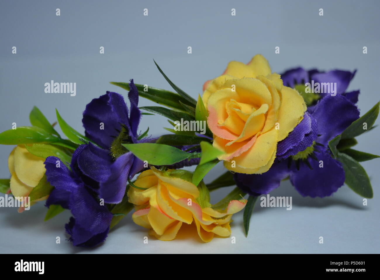 Interessante Haardekoration für Frauen, festlicher Look. Schöner Kopfreif aus blauen, gelben Blumen und grünen Blättern auf weißem Hintergrund. Stockfoto