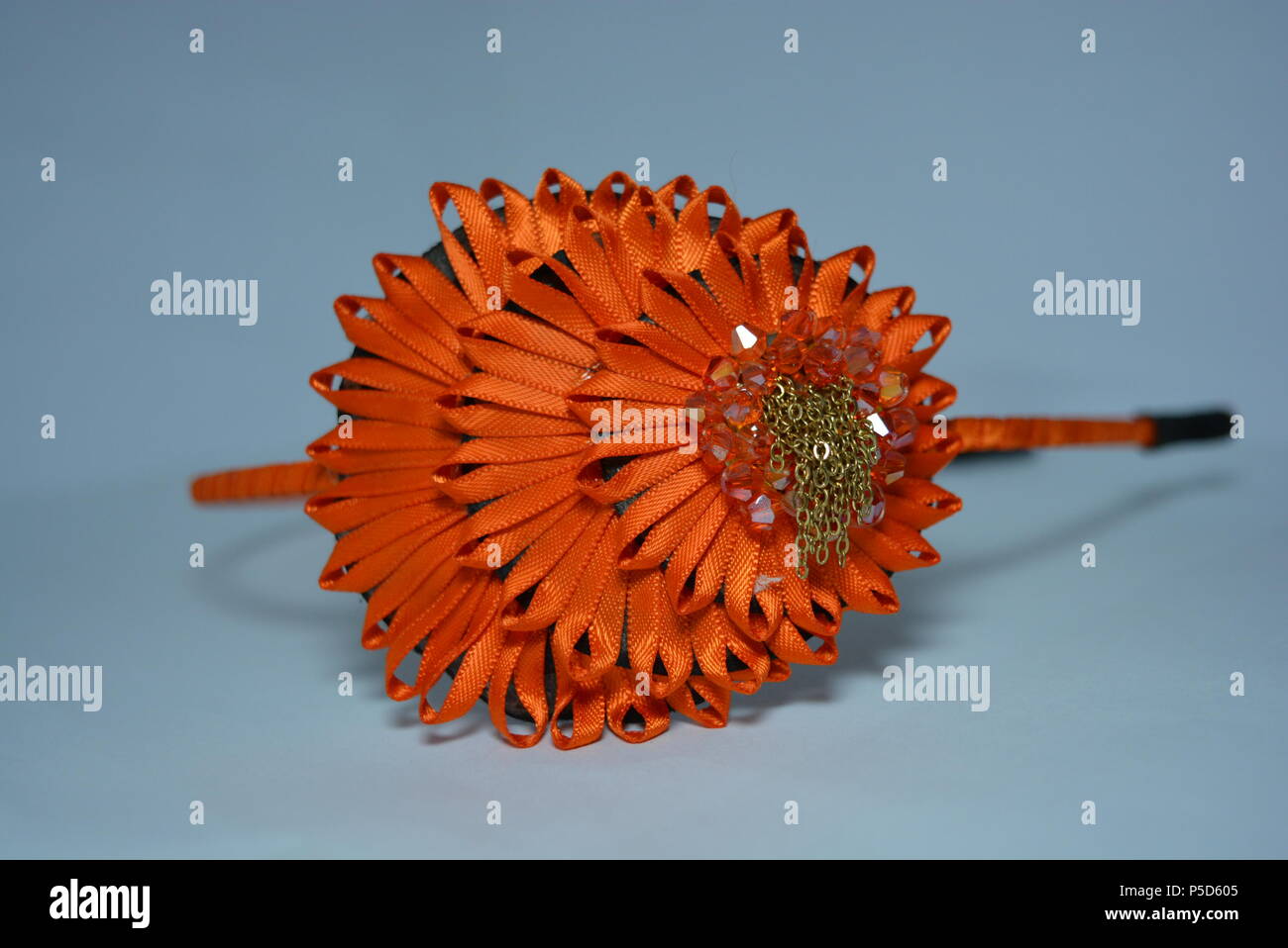 Interessante Haardekoration für Frauen, festlicher Look. Schöner Kopfreif aus Stoff aus orangefarbenem Glanzband mit stilvoller Dekoration auf weiß. Stockfoto