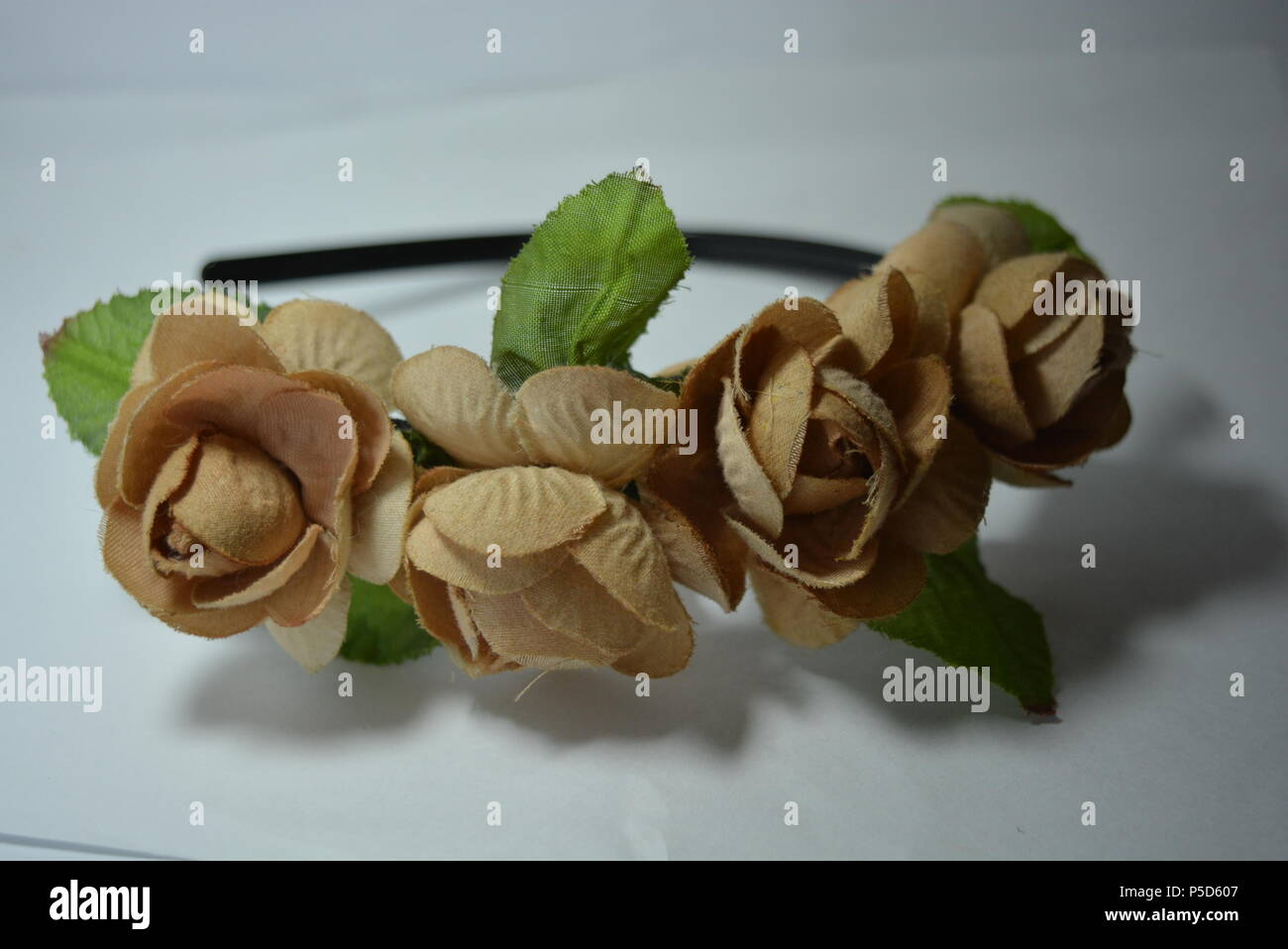 Interessante Haardekoration für Frauen, festlicher Look. Schöner Kopfreif aus beigen Blumen und grünen Blättern auf weißem Hintergrund. Stockfoto