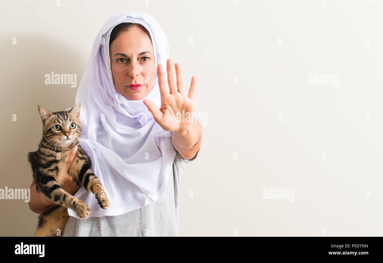 1001 Frau tragen weiße hijab Halten einer Katze mit der offenen Hand tun, STOP-Schild mit ernsten und selbstbewussten Ausdruck, Verteidigung Geste Stockfoto