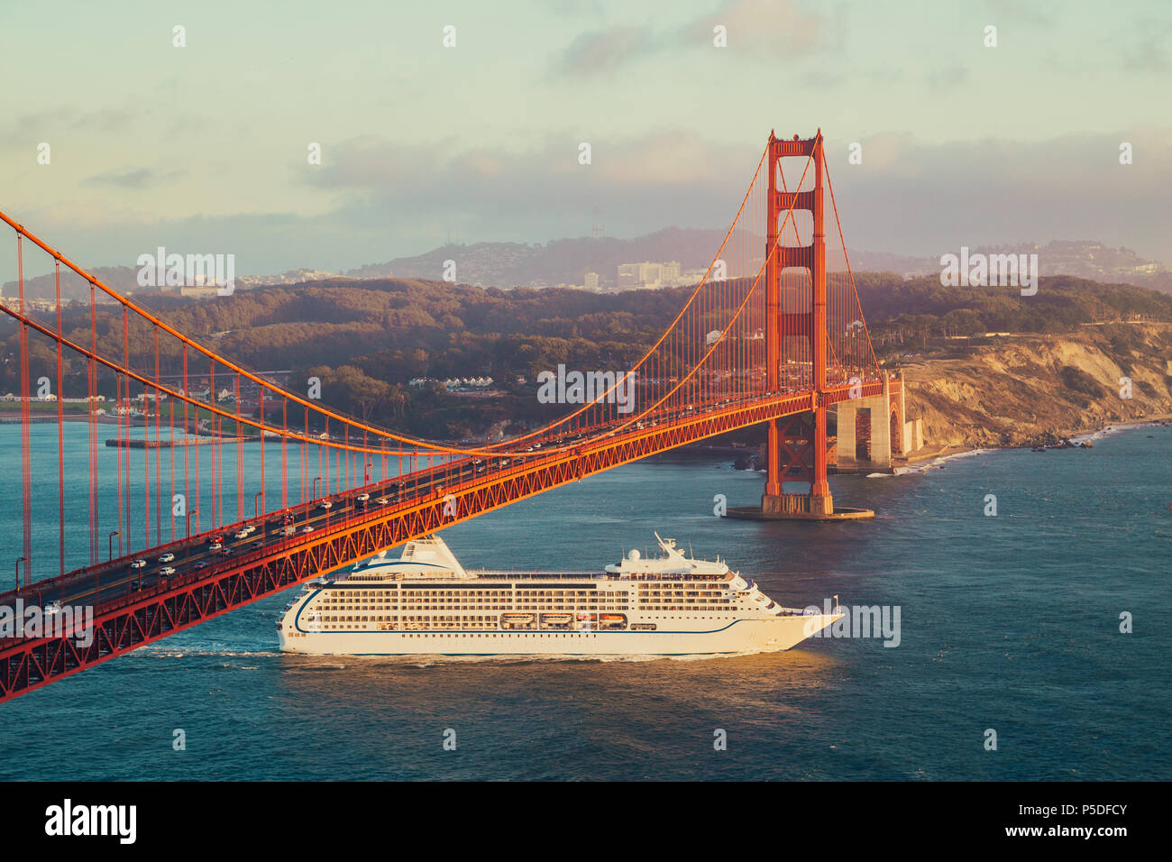 Schönen Panoramablick auf Kreuzfahrtschiff, die berühmte Golden Gate Bridge mit Blick auf die Skyline von San Francisco im Hintergrund in wunderschönen goldenen Eveni Stockfoto