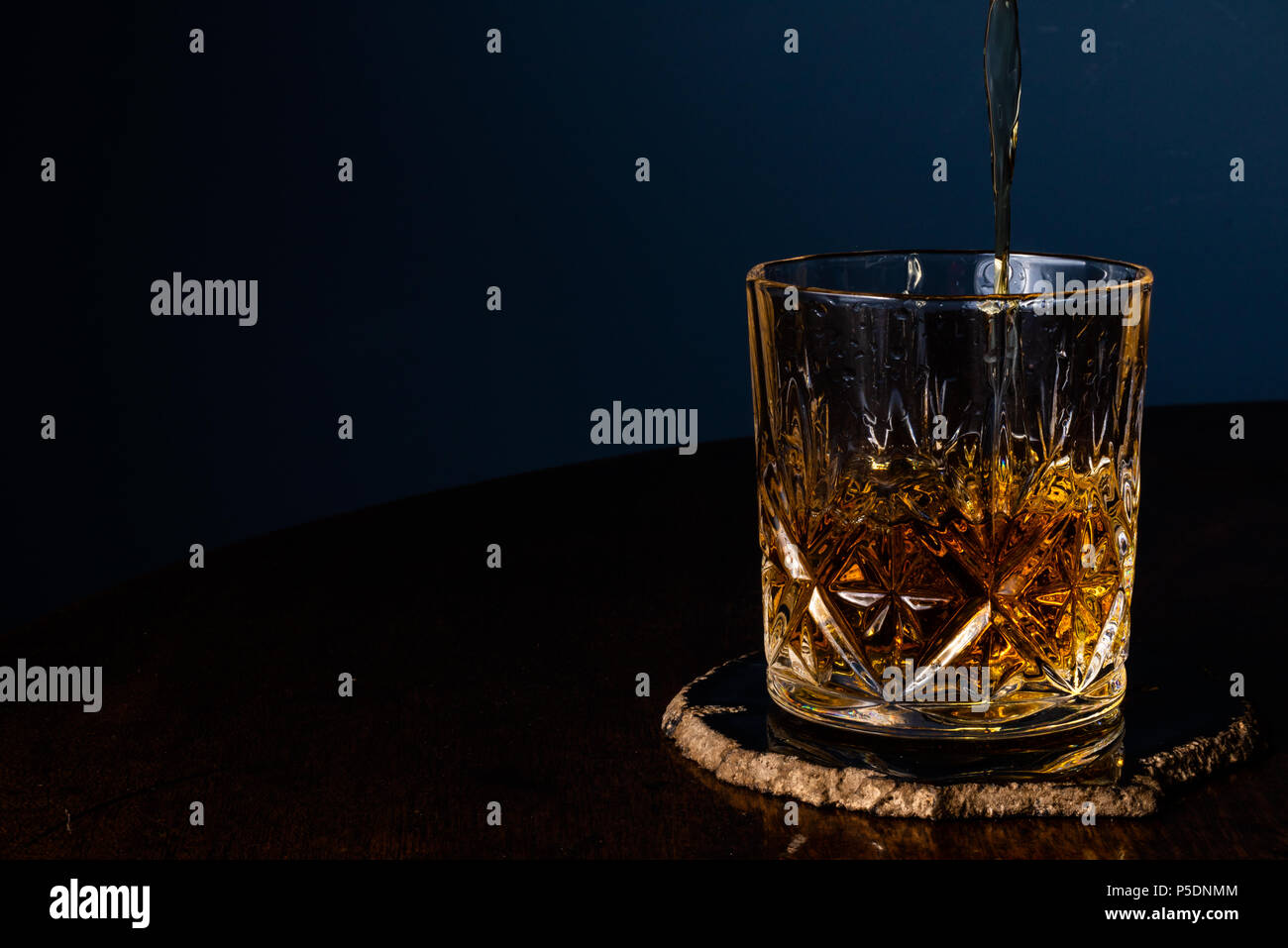 Whiskey in einem Kristall Tumbler auf einem dunklen Holztisch mit einem blauen Hintergrund gegossen. Stockfoto