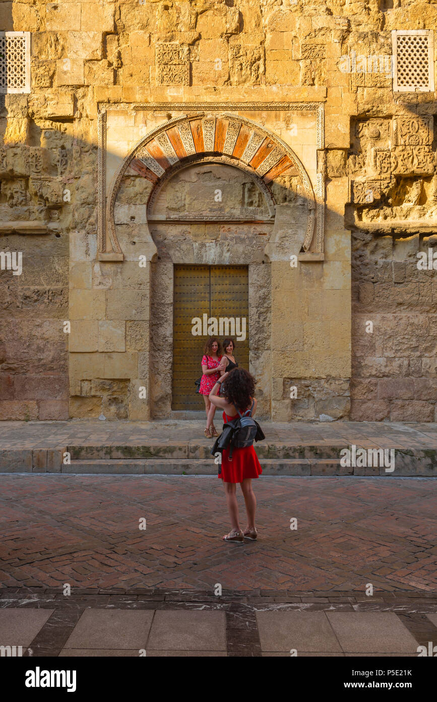 Junge Frauen, eine junge Frau fotografiert ihre Freunde, die vor einer maurischen Tür in der Außenwand der Mezquita, Cordoba, Spanien, posierten. Stockfoto