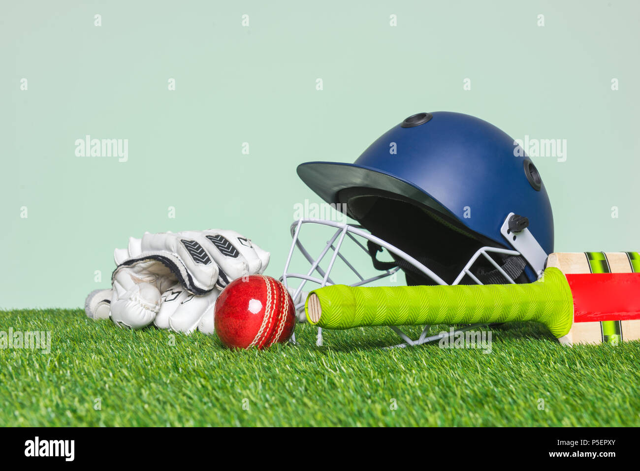 Cricket Equipment mit Schläger, Ball, Helm und Handschuhe auf Gras mit grünem Hintergrund. Stockfoto