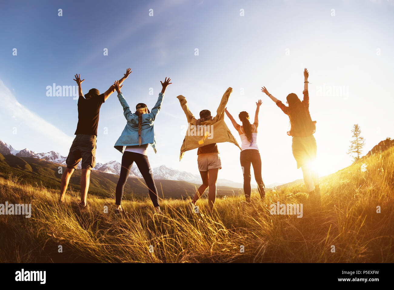 Gruppe der glücklichen Freunde steht gegen Berge Sonnenuntergang mit erhobenen Armen und Spaß Stockfoto