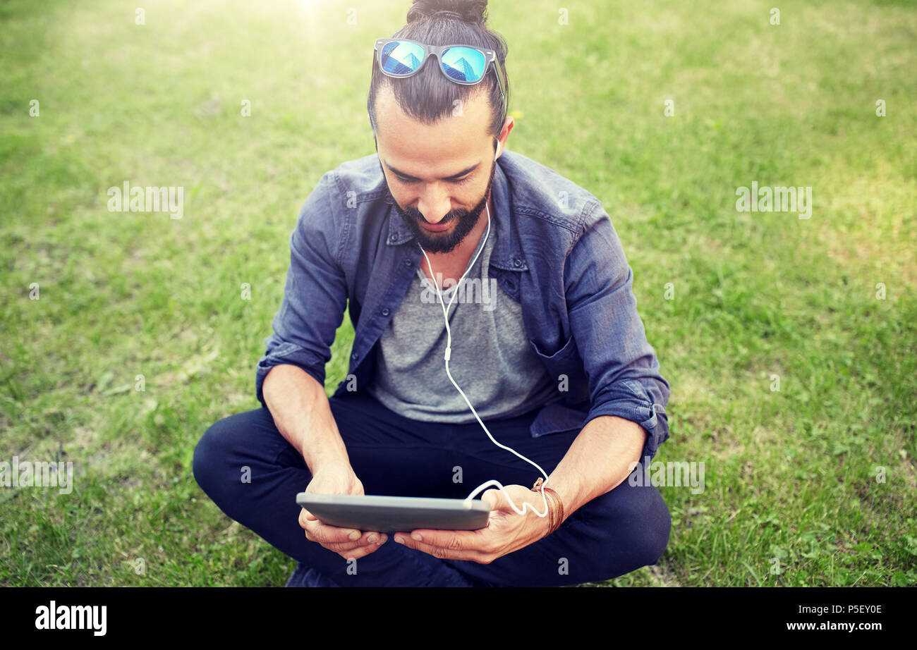 Mann mit Kopfhörern und Smartphone sitzen auf Rasen Stockfoto