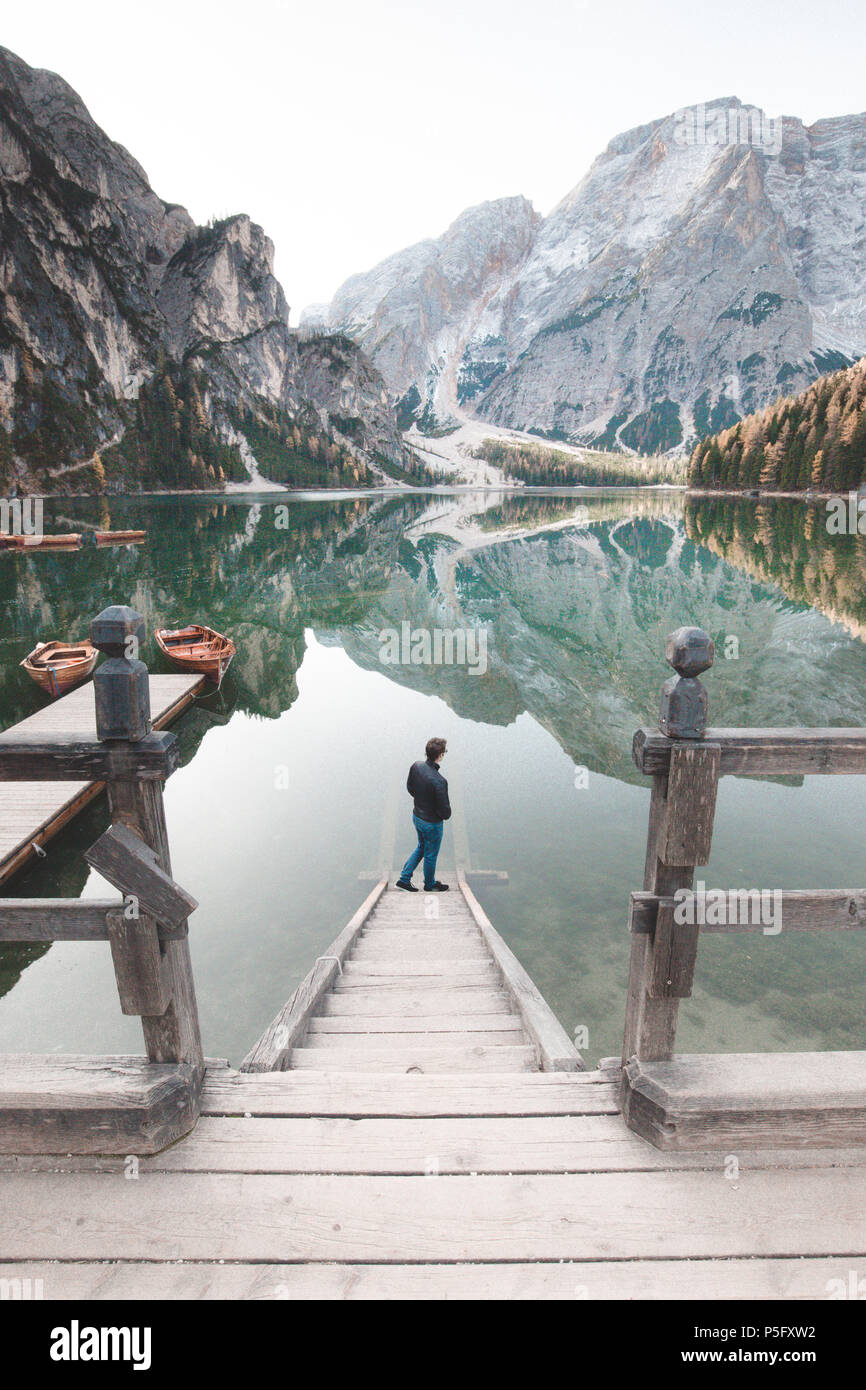 Wunderschöne Aussicht auf einen jungen Mann stehen auf hölzernen Treppen den Sonnenaufgang an der berühmten Lago di Braies Dolomiten, Südtirol, Italien Stockfoto