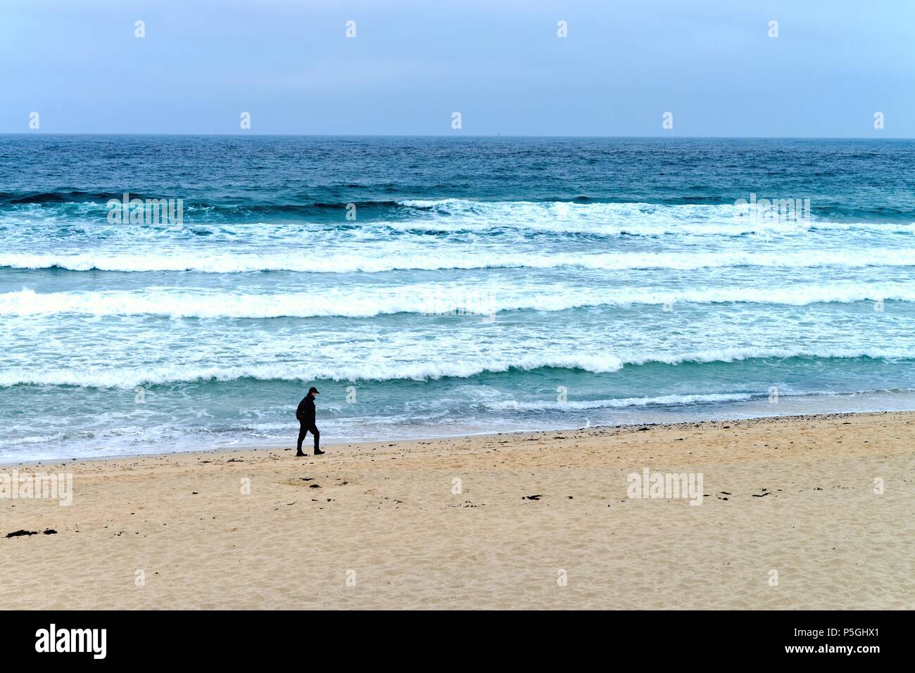 Solitary Man entlang eine Sandstrand mit brechenden Wellen im Hintergrund St. Ives in Cornwall, England, Großbritannien Stockfoto