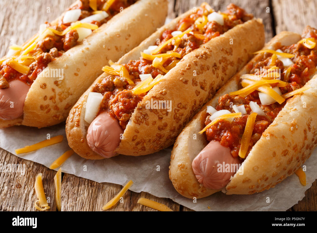 Authentische Chili Hot Dog mit Cheddar Käse, Zwiebel und pikanter Sauce close-up auf Papier auf dem Tisch. Horizontale Stockfoto