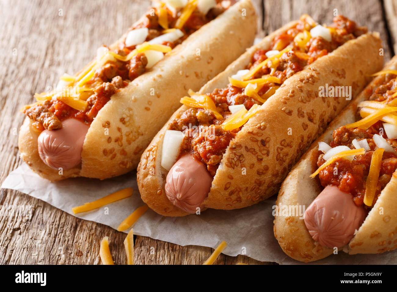 American fast food: Chili Hot Dogs mit Cheddar Käse, würzigen Fleisch Hackfleisch, Zwiebel und Sauce close-up auf dem Tisch. horizontal, rustikalen Stil Stockfoto