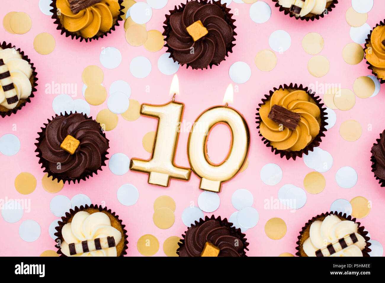 Nummer 10 gold Kerze mit Cupcakes gegen ein Pastell rosa Hintergrund Stockfoto