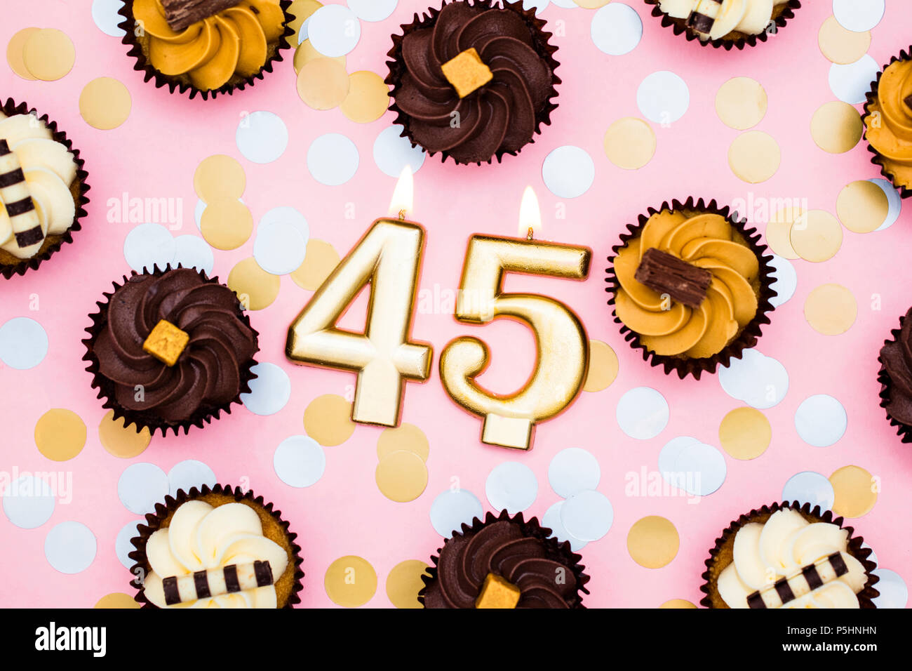 Nummer 45 gold Kerze mit Cupcakes gegen ein Pastell rosa Hintergrund Stockfoto