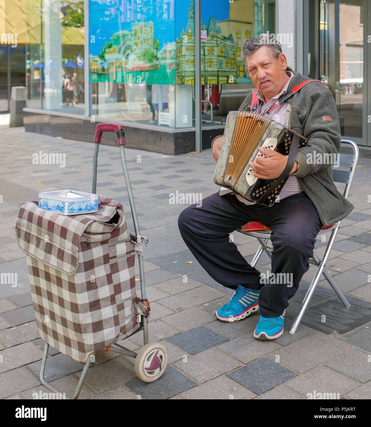 Eine sitzende Gaukler spielen auf dem Knopfakkordeon in der Sauchiehall Street, Glasgow, Schottland, Vereinigtes Königreich Stockfoto