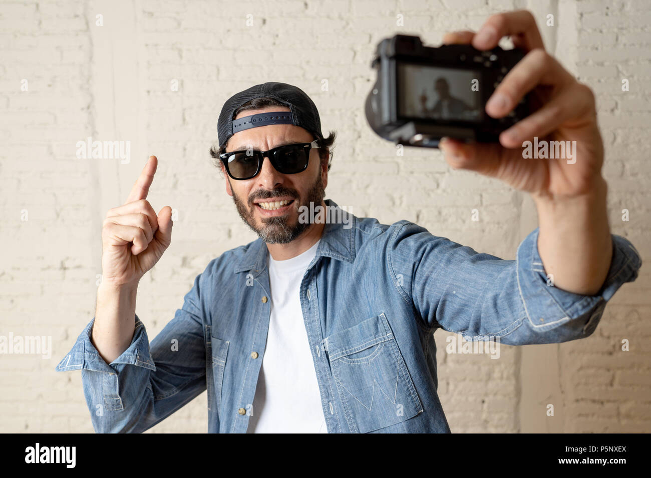 Jungen attraktiven Mann legere Kleidung, Sonnenbrillen in Hipster style moderne Optik holding Foto Kamera schießen self portrait selfie Bild oder Reco Stockfoto