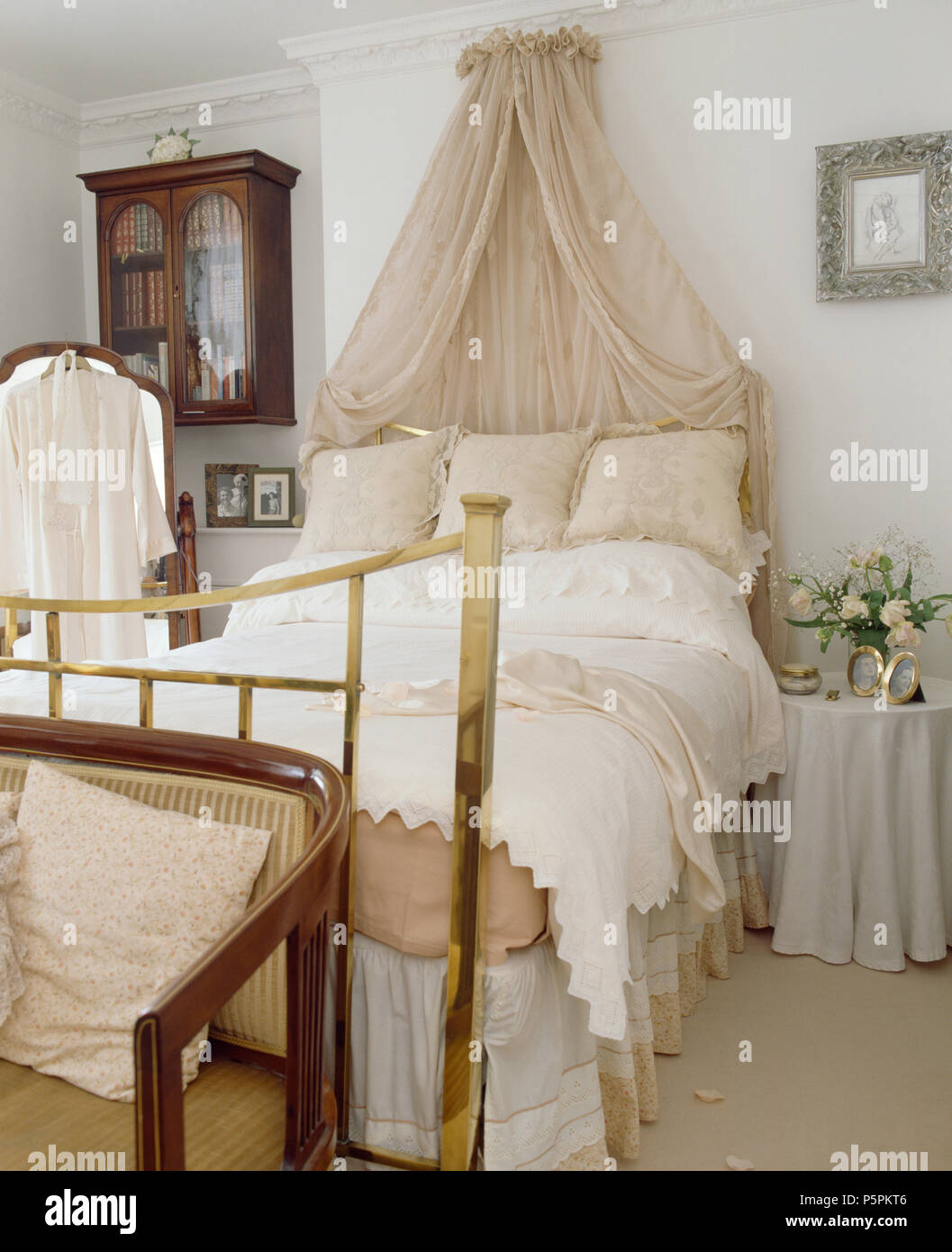 Coronet mit cremefarbenen voile Gardinen über dem Bett aus Messing mit  Creme Bettwäsche im Land Schlafzimmer Stockfotografie - Alamy