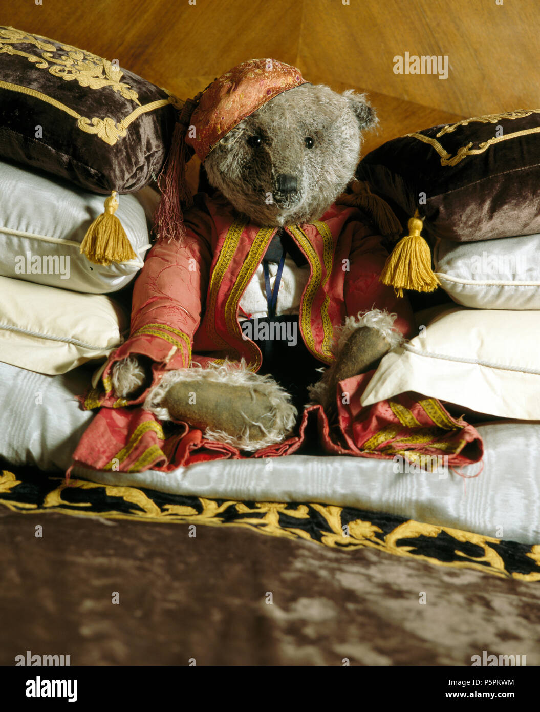 Alte Teddybär in Vintage Kleidung mit Stapel des Samtkissen gekleidet Stockfoto