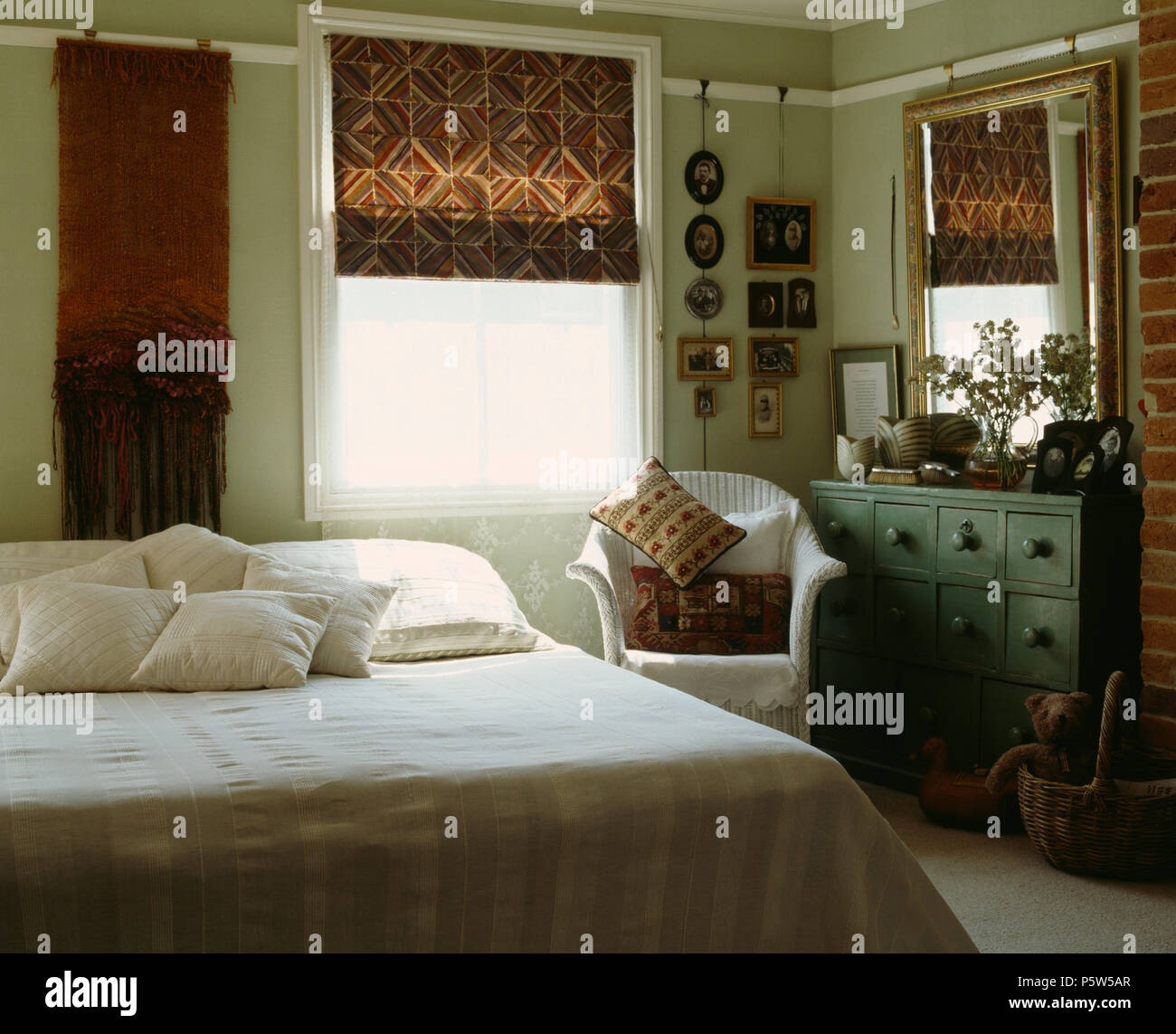 Blind auf Fenster in traditionellen Schlafzimmer Gemusterten mit gemalten Lloyd-Loom Sessel neben dem Bett mit weißer Bettwäsche Stockfoto
