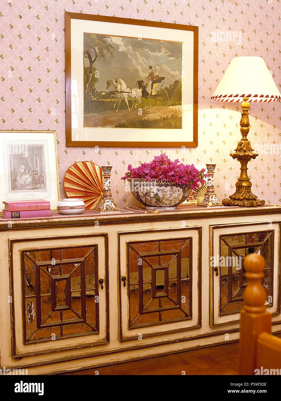 Reich verzierte Anrichte mit beleuchteten Messing Lampe im Schlafzimmer mit rosa Tapete Stockfoto