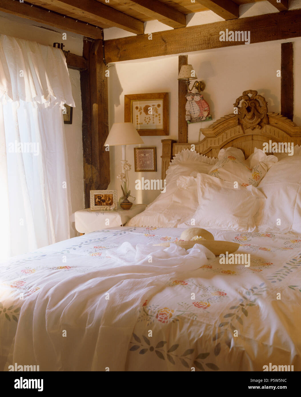 Lace-umrandete Kissen und Stenciled Decke auf dem Bett im Cottage Schlafzimmer mit weißer Baumwolle Vorhänge am Fenster Stockfoto