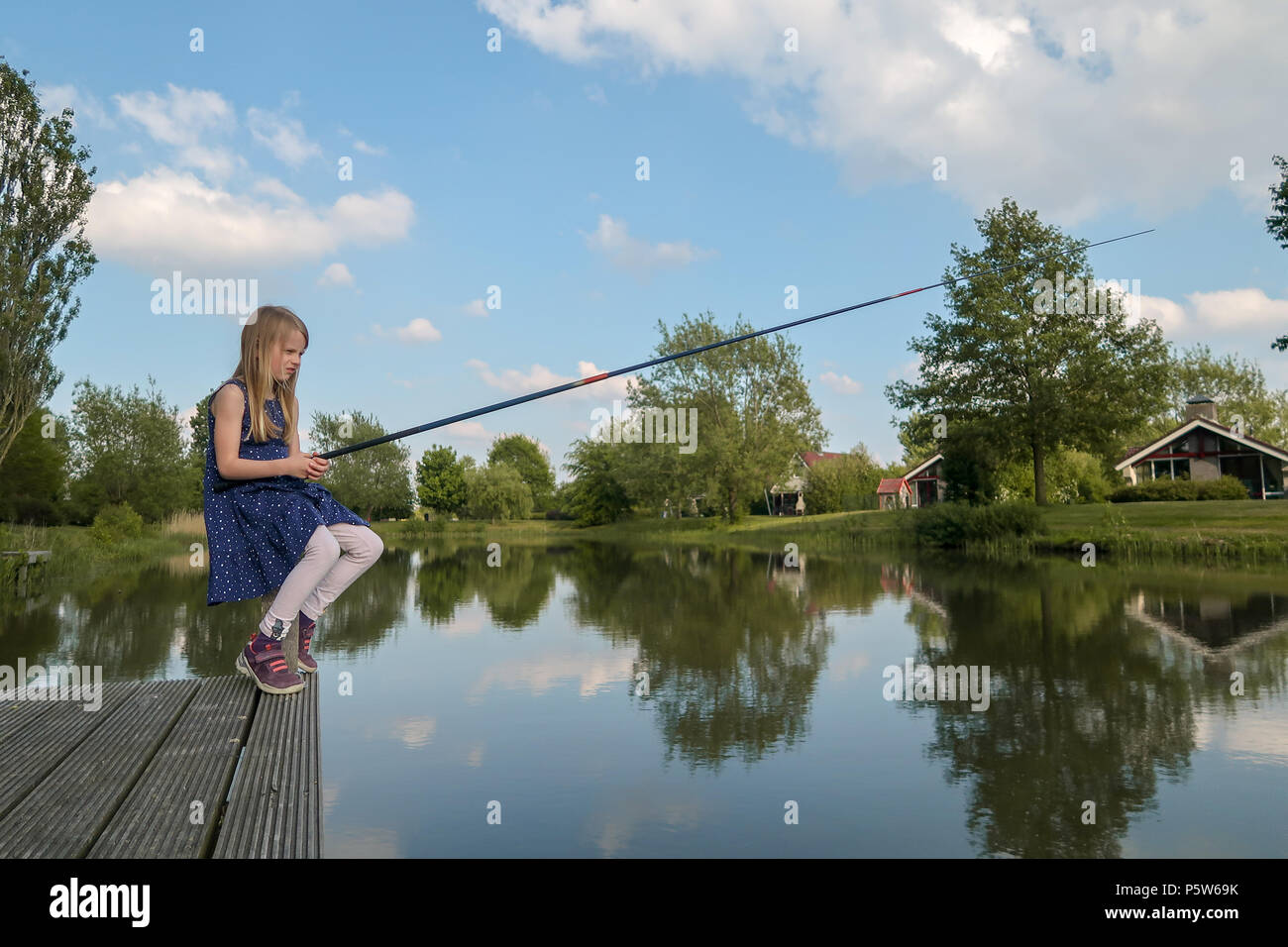 Ein 7 Jahre altes Mädchen sitzt an einem See mit Angelrute und Blick auf das Wasser. Sie wartet auf einen Fisch zu beißen Stockfoto