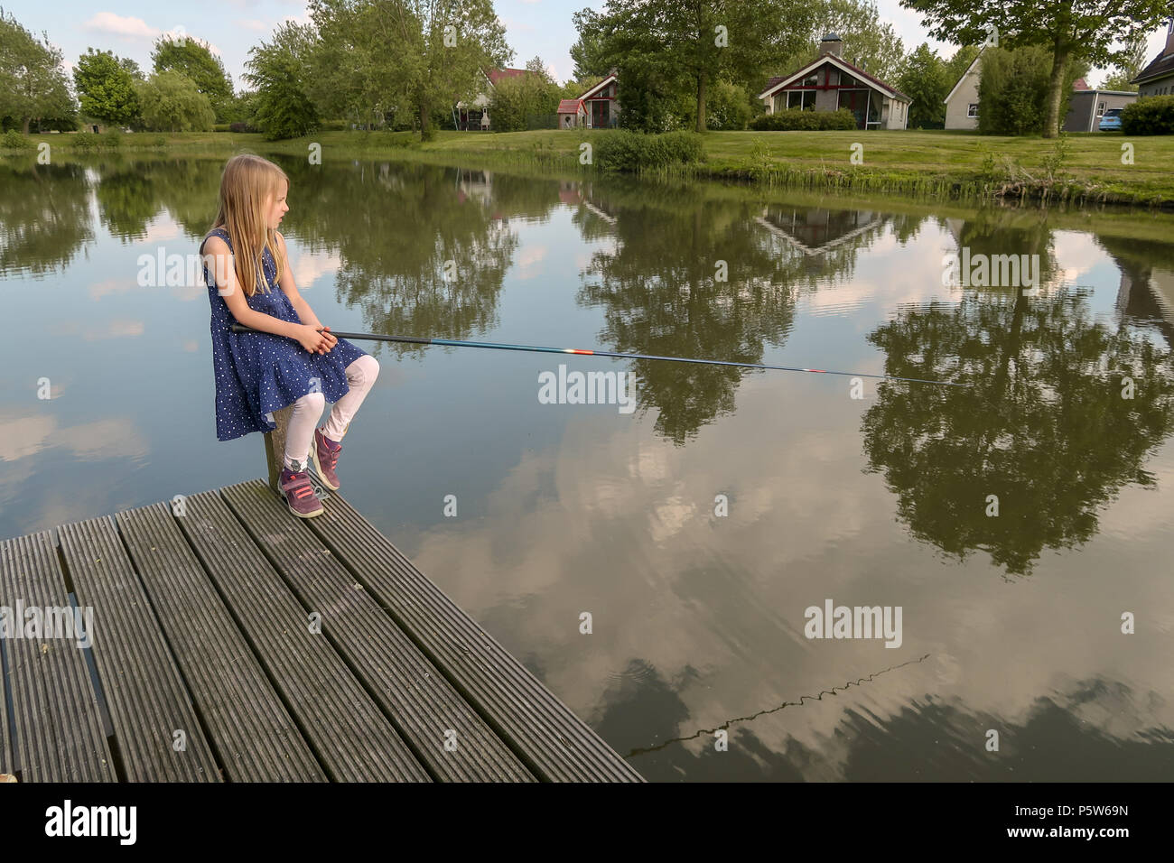 Ein 7 Jahre altes Mädchen sitzt an einem See mit Angelrute und Blick auf das Wasser. Sie wartet auf einen Fisch zu beißen Stockfoto