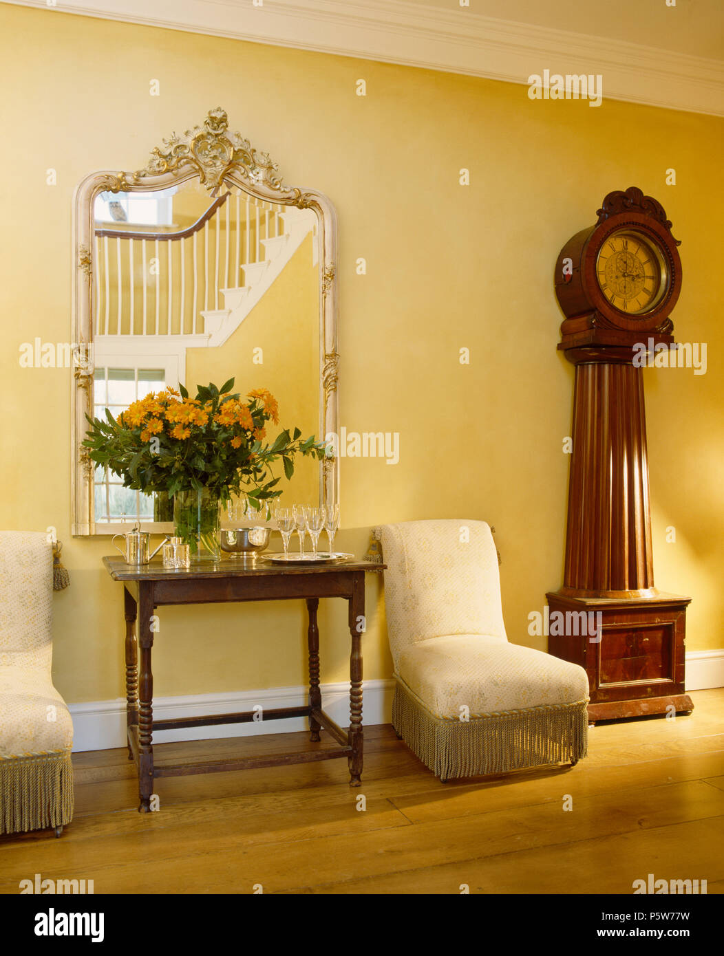 Reich verzierten Spiegel über Console Tabelle im Land Halle mit antiken Lange-Uhr und gepolsterte Stühle Creme Stockfoto