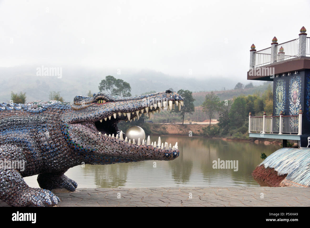 Am blauen und silbernen Krokodil Holding eine silberne Kugel in den Mund an einem nebligen Morgen im Wat Pa Huai Lat (Tempel) im Norden von Thailand Stockfoto