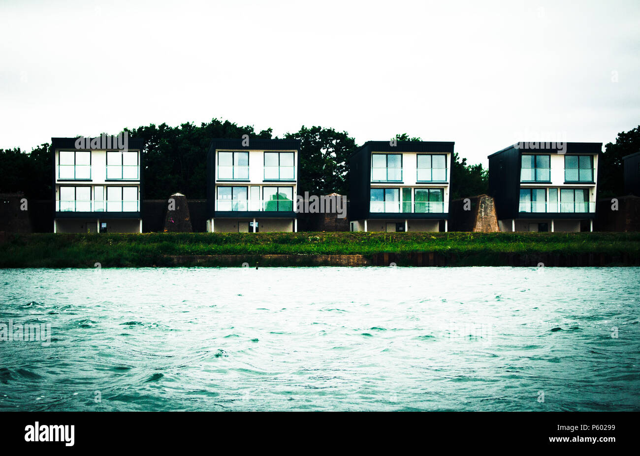 Square House Pads in einer Reihe am Rand eines Sees mit Wasser im Vordergrund. Stockfoto
