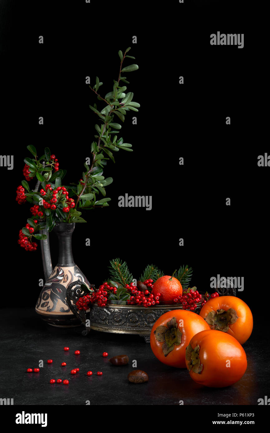 Stilleben mit Früchte fallen als kakipflaume, Kastanien und Mandarin orange, mit roten Beeren dekoriert. Stockfoto
