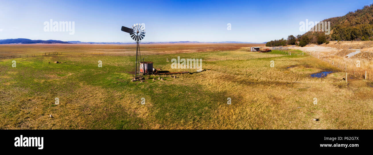 Flache Ebene von Dry Lake George in NSW und Akt der Australien Open mit Rinder Farm und remote einzelne Mühle gegen den blauen Himmel. Stockfoto