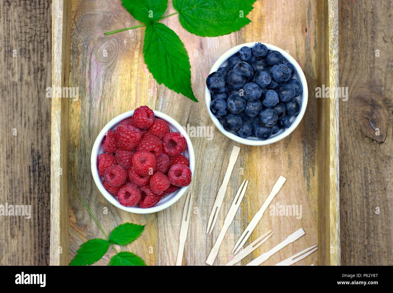 Gesunde Lebensmittel, Landwirtschaft, Ernte und Früchte Konzept: frische reife Heidelbeeren und Himbeeren in zwei Schalen auf einem hölzernen Fach. Stockfoto