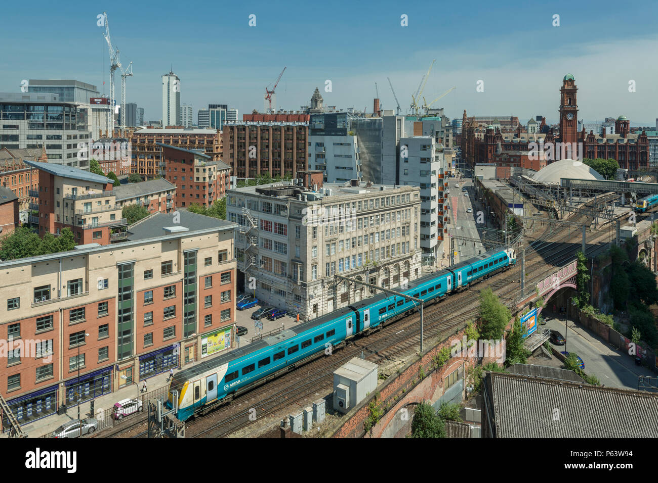 Ein Arriva Zug kommt an Bahnhof Oxford Road in Manchester, mit der Skyline der Stadt im Hintergrund. Stockfoto