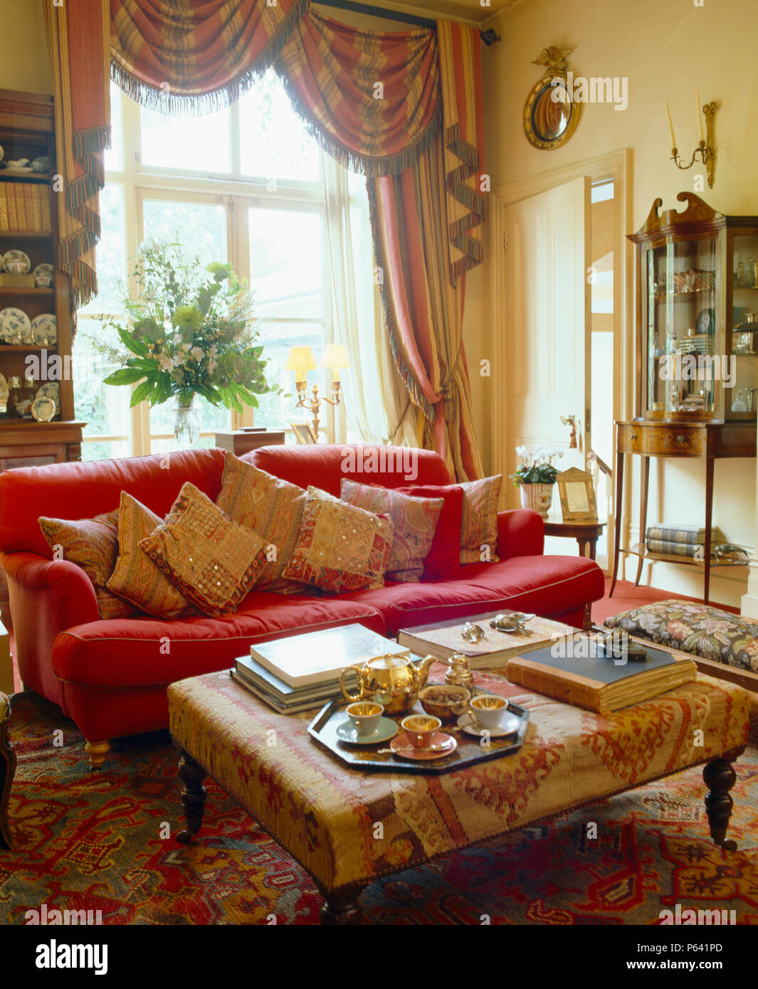 Die gepolsterten Hocker, Couchtisch neben komfortablen rosa Sofa im Wohnzimmer mit Gerafften + tailed Vorhänge Stockfoto