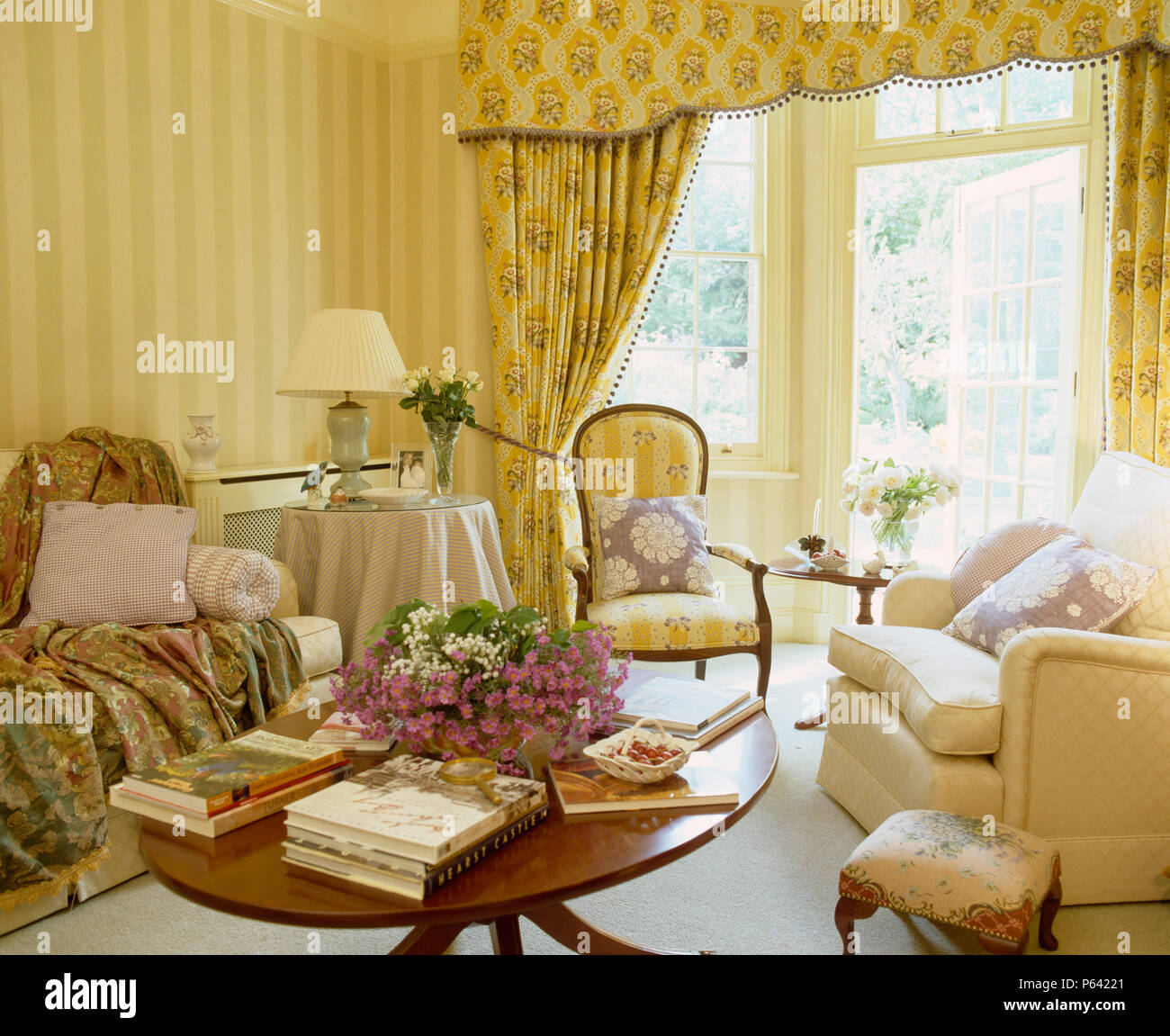 Pierre Frey Vorhänge an den Fenstern im Wohnzimmer mit gelb gestreifte Tapeten und antiken Tisch Stockfoto