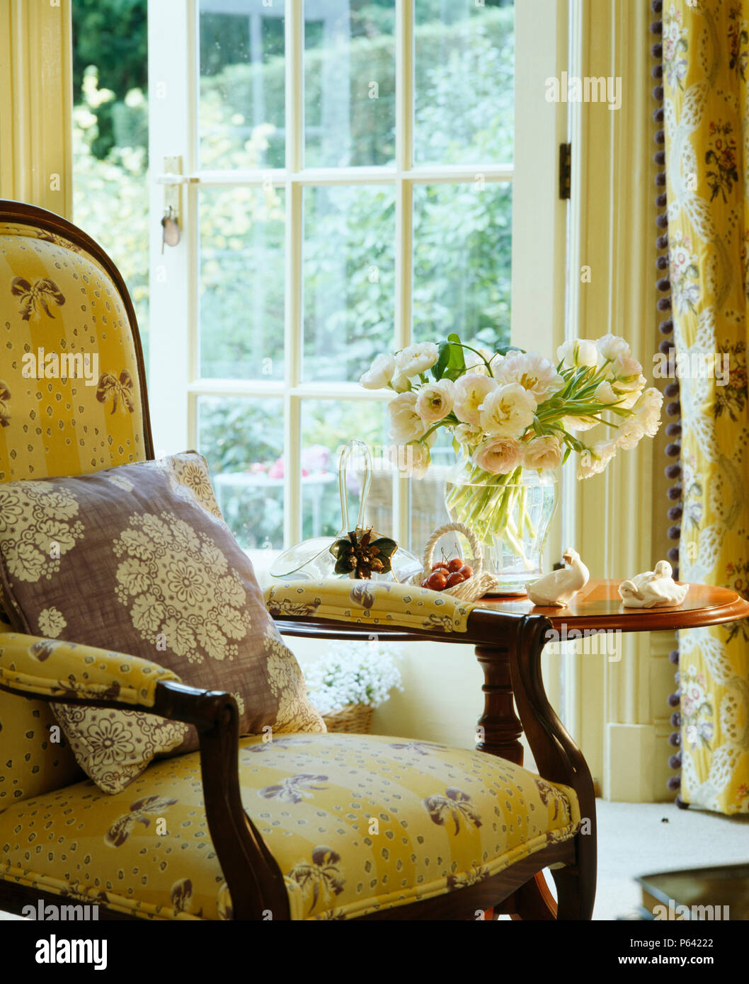 Viktorianische Sessel in Hellgelb Pierre Frey gepolstert neben kleinen antiken Tisch vor französischen Fenstern Stockfoto