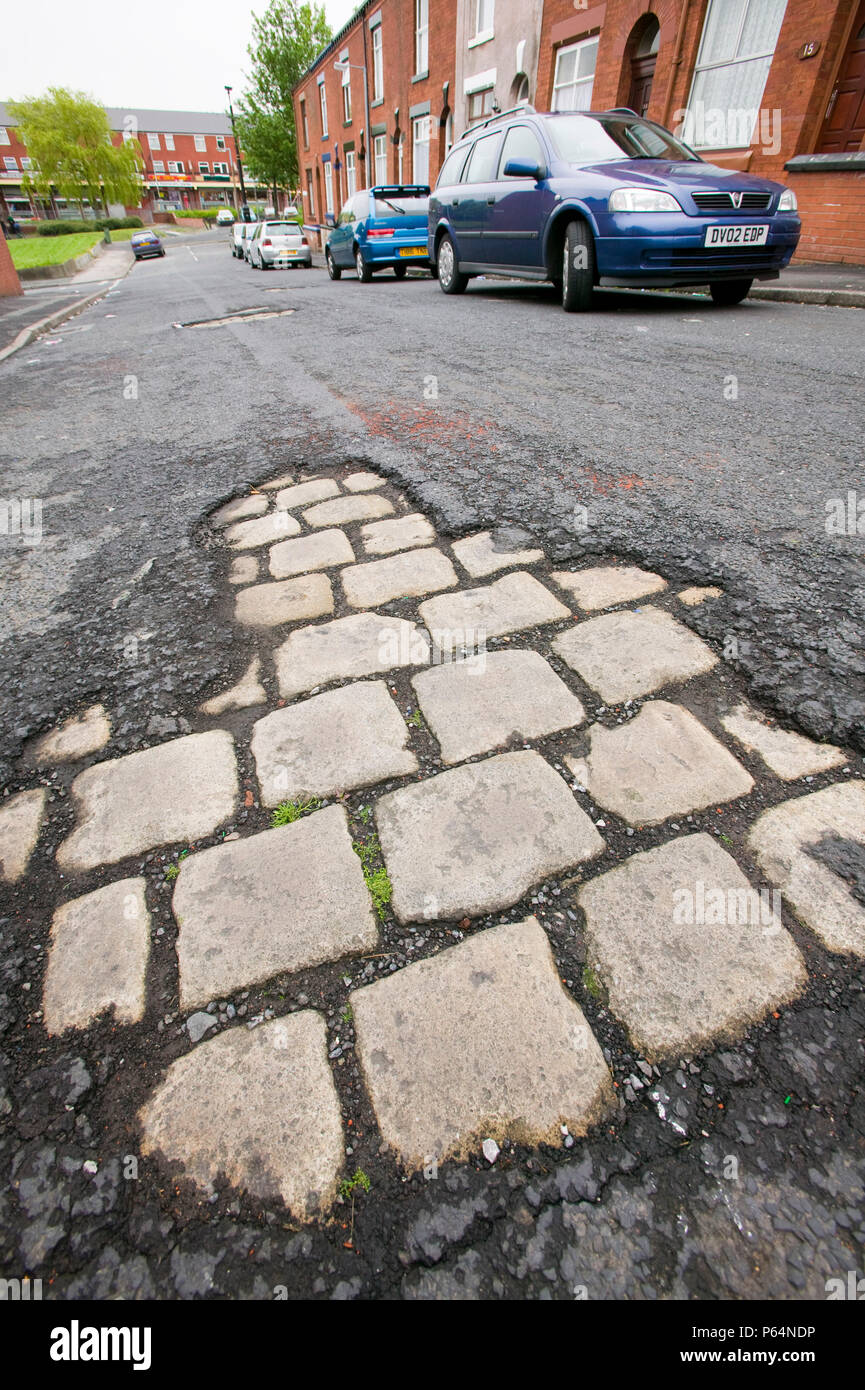 Altes Kopfsteinpflaster offenbart unter Asphalt auf eine Oldham Street Lancashire UK Stockfoto