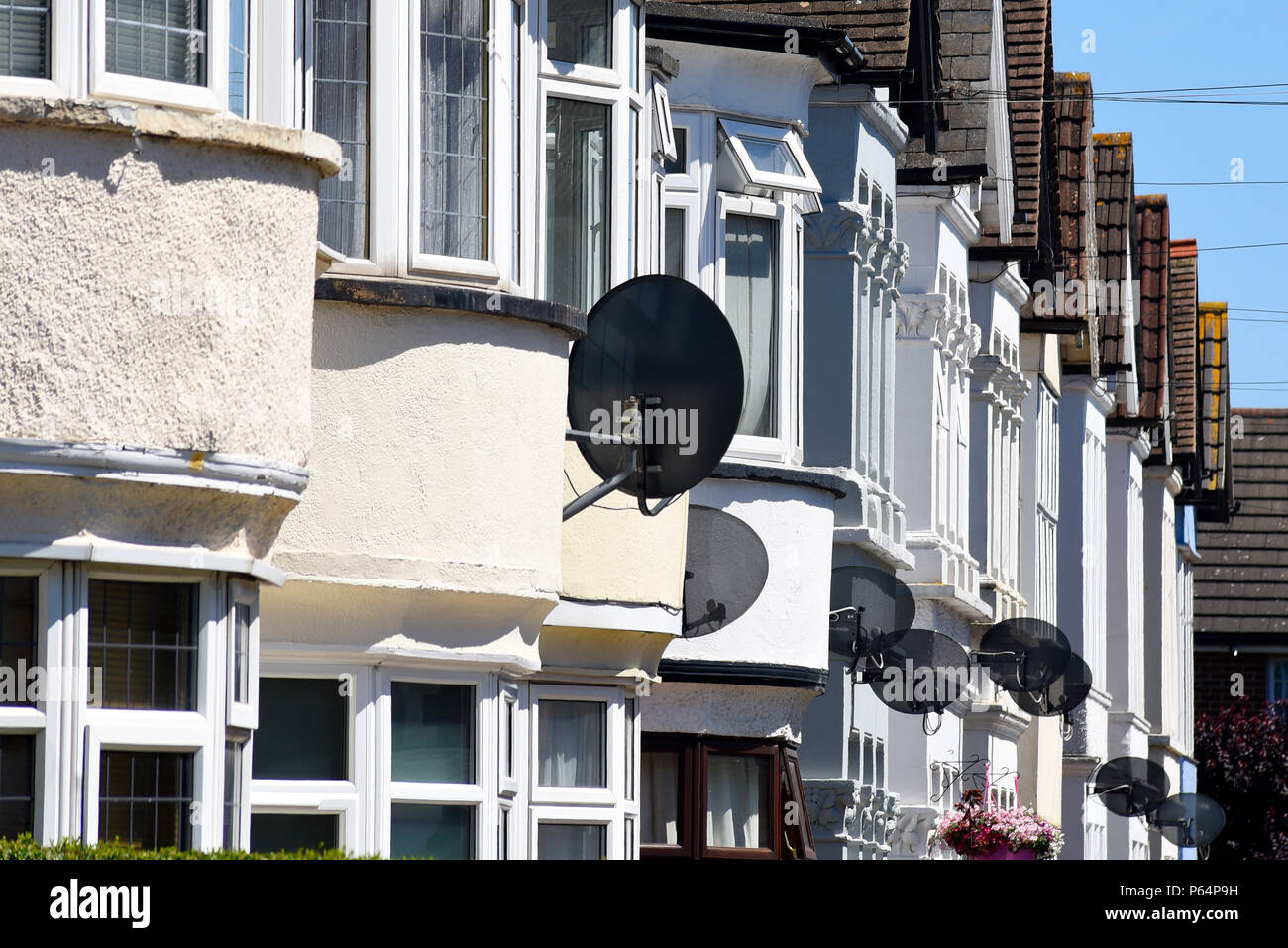 Reihe von Satellitenschüsseln extern montiert auf Reihe von weißen Häusern. Sat-TV-Receiver auf Erkerfenster. Westcliff On Sea, Essex, Großbritannien Stockfoto
