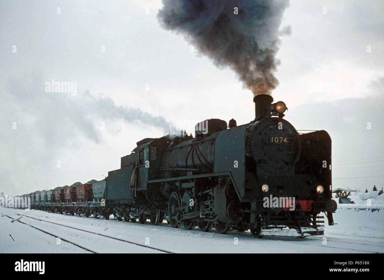 Eine geladene Kies Zug von Raagarvi nördlich des Polarkreises zu Rovanemi durch den Finnischen Eisenbahnen 2-8-2 Mikado Klasse TR1 Nr. 1074 im März 1972 leitete. Stockfoto